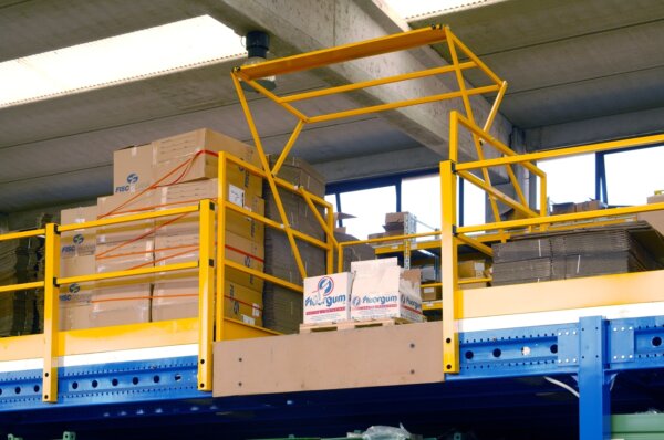 Sas de sécurité jaune sur une plateforme élevée dans un entrepôt industriel, entouré d’étagères bleues remplies de marchandises